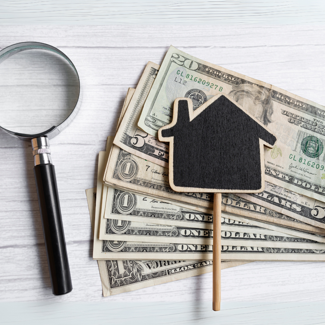 Une loupe et une maquette de maison en bois posées sur des billets de banque, symbolisant l'évaluation du prix d'un immeuble de rapport